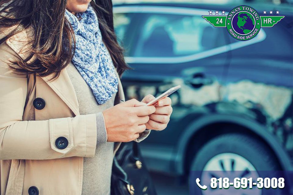 Call-West-Hollywood-Towing-For-a-Quick-Response A woman is looking at her phone while standing next to a car.