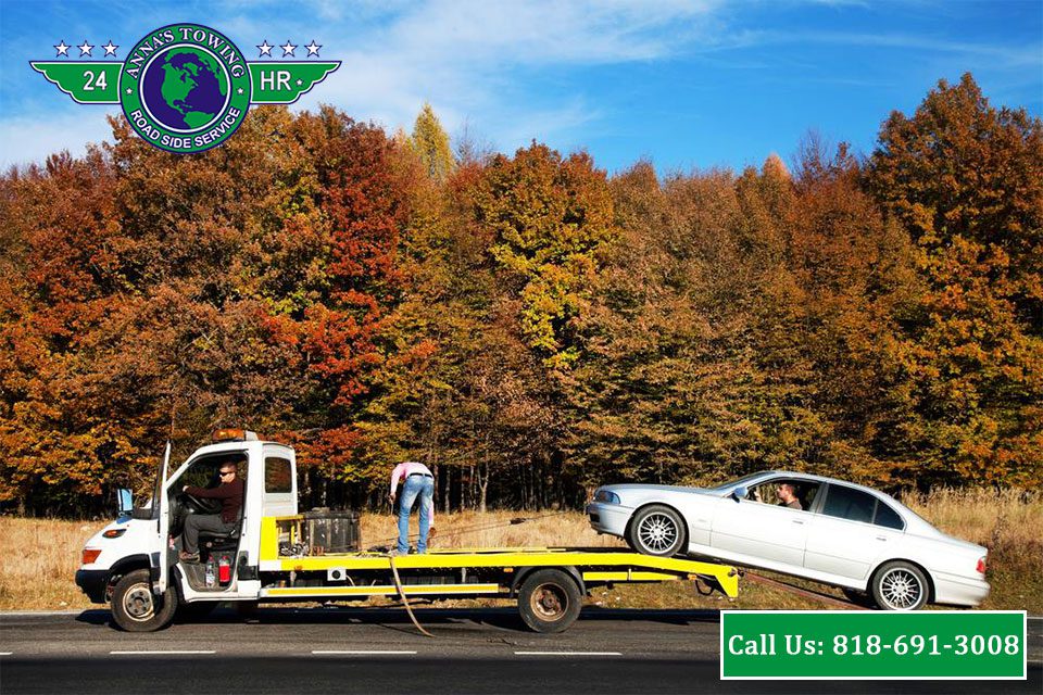 Valley-Village-Towing-Tips-On-How-To-Call-Roadside-Assistance-When-It’s-Raining A tow truck towing a white car on the side of a road.
